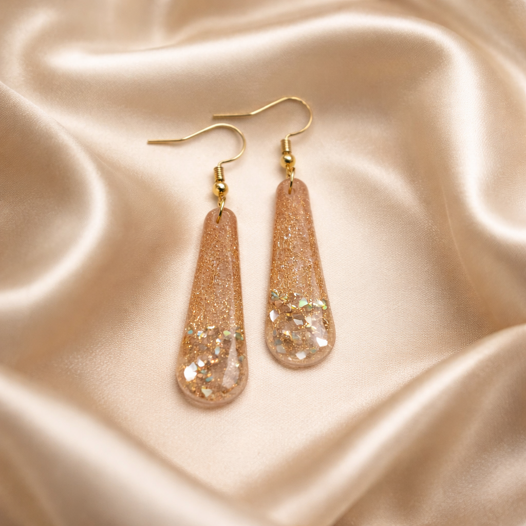 Pink and gold drop earrings with glittery details on a soft background