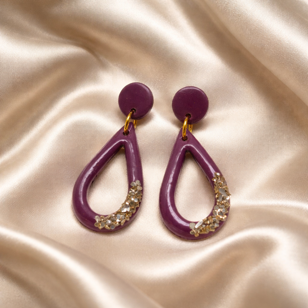 Two purple drop earrings with sparkling accents on a silky background.