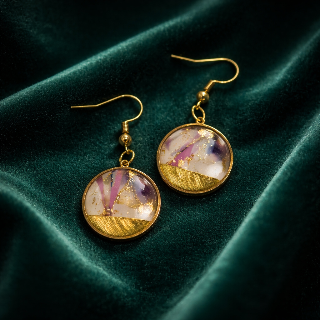 Handmade purple and white marble earrings with gold accents on a green surface