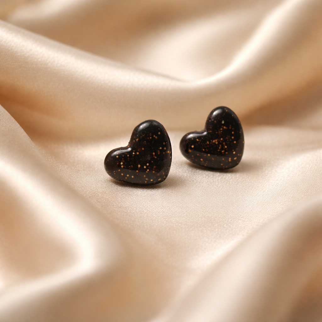 Black heart stud earrings with copper speckles on champagne fabric