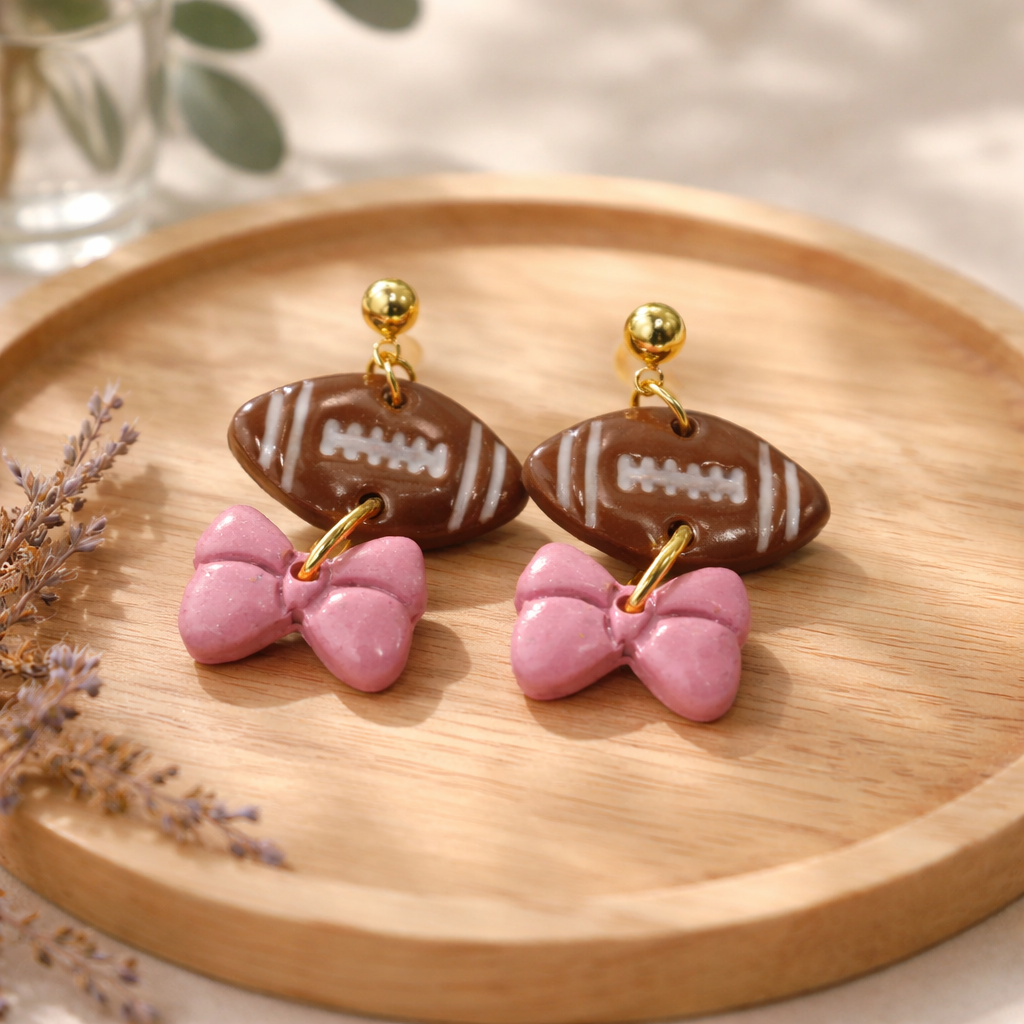 Brown football dangle earrings with glossy pink bow charms and gold studs