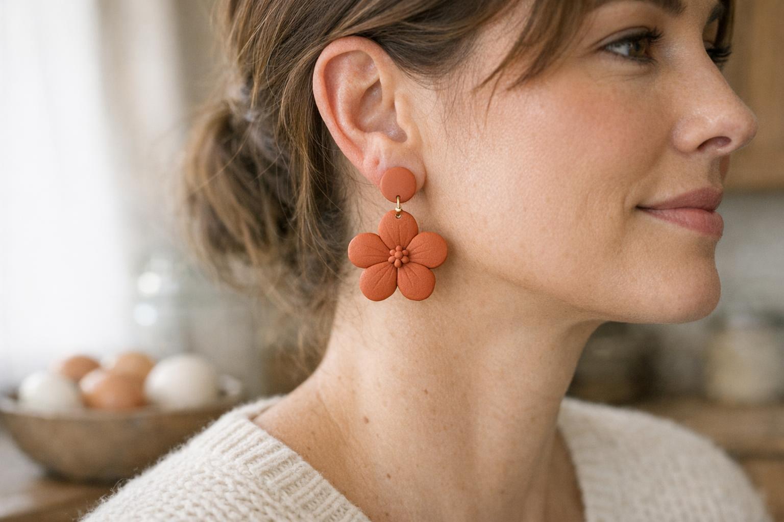 Woman wearing matte terracotta teardrop polymer clay earrings with a cream sweater in a cozy farmhouse kitchen.